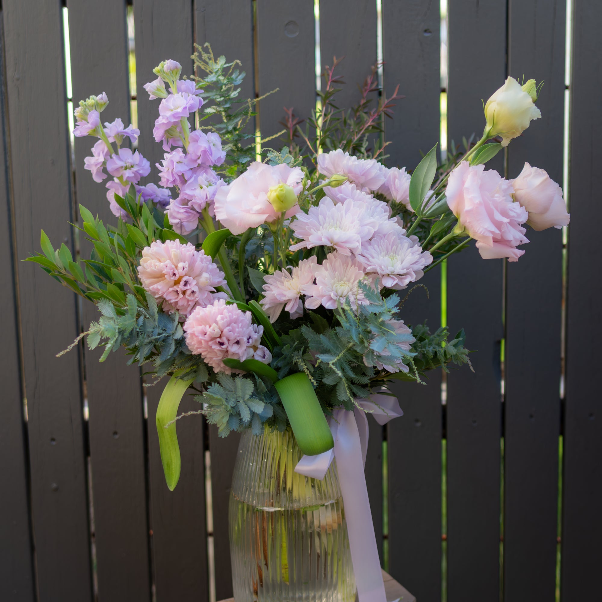 Blush and lavender Mother's Day flower arrangement in ribbed glass vase with satin ribbon, featuring chrysanthemums, hyacinth, lissianthus and stock