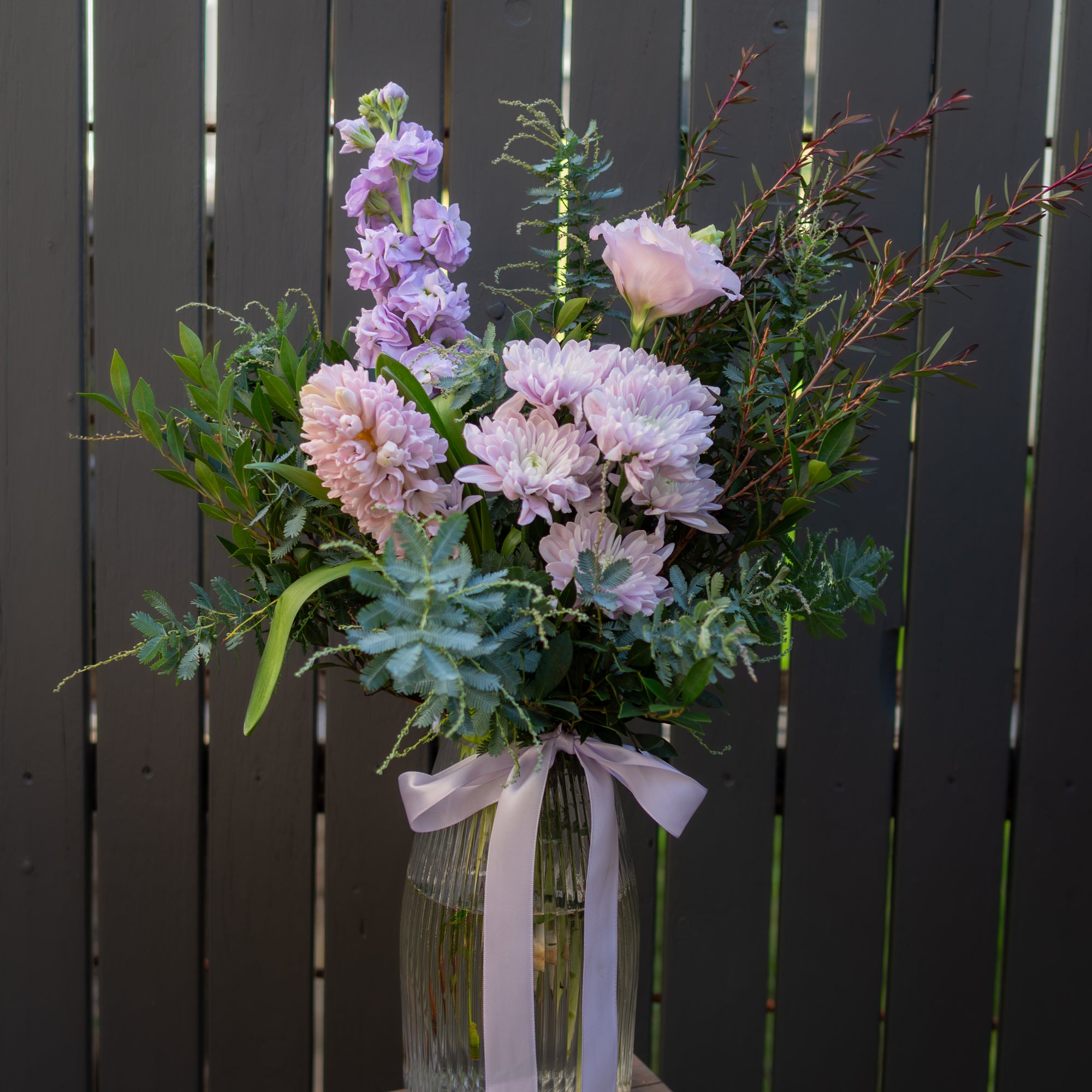 Blush and lavender Mother's Day flower arrangement in ribbed glass vase with satin ribbon, featuring chrysanthemums, hyacinth, lissianthus and stock