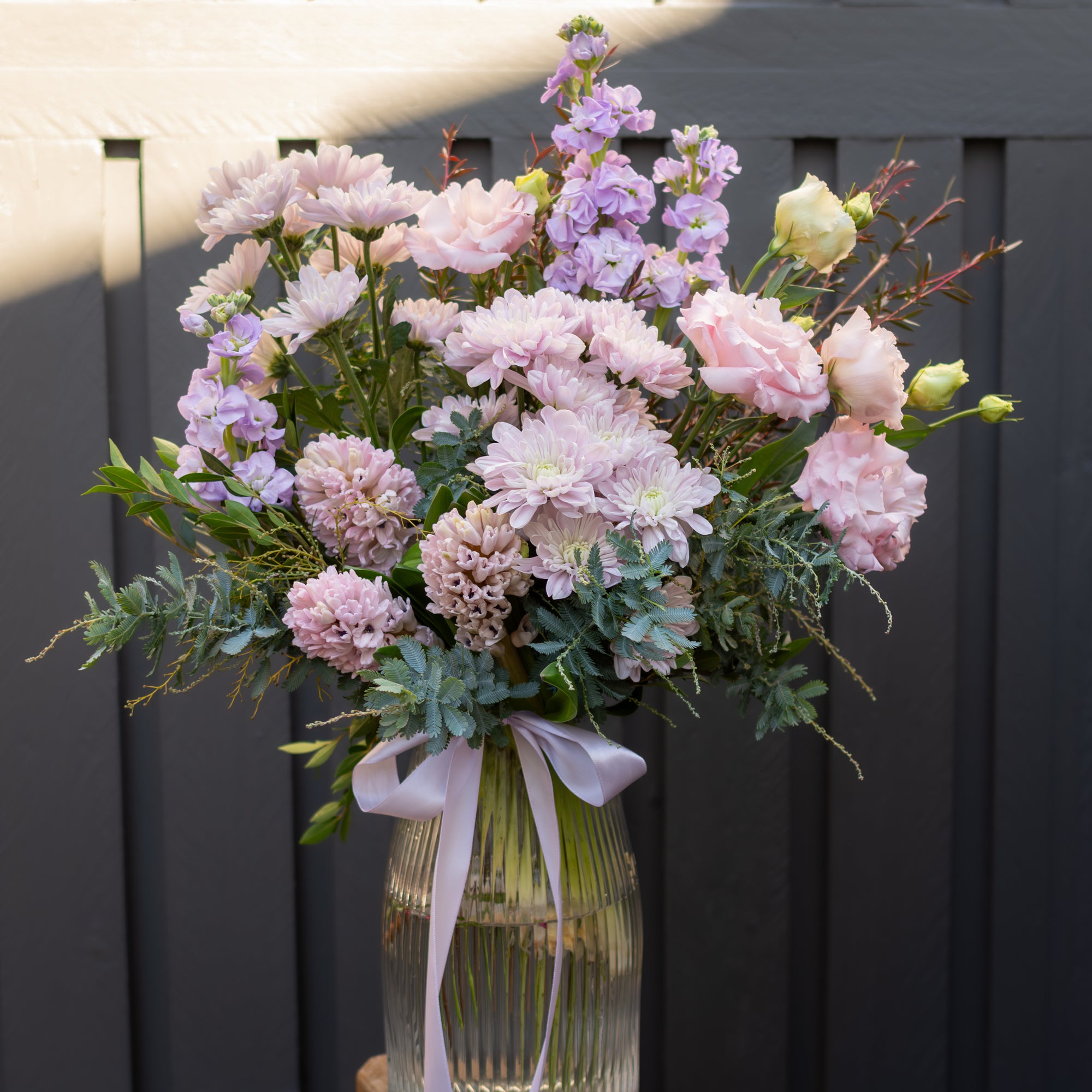 Blush and lavender Mother's Day flower arrangement in ribbed glass vase with satin ribbon, featuring chrysanthemums, hyacinth, lissianthus and stock